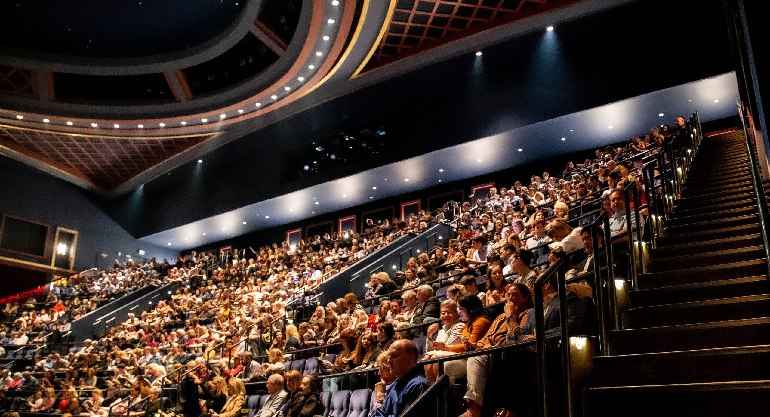 Full crowd of people sitting in the auditorium seating conversing with eachother